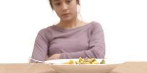 Una ragazza di fronte a un piatto di pasta. I disturbi del comportamento alimentare si manifestano attraverso alcuni comportamenti specifici spesso combinati tra loro, come la restrizione delle calorie assunte, una costante attenzione al peso e all’immagine del proprio corpo, e il controllo del cibo per gestire emozioni e pensieri negativi. 