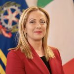 Una foto ufficiale di Giorgia Meloni sorridente con la bandiera dell'Italia alle spalle