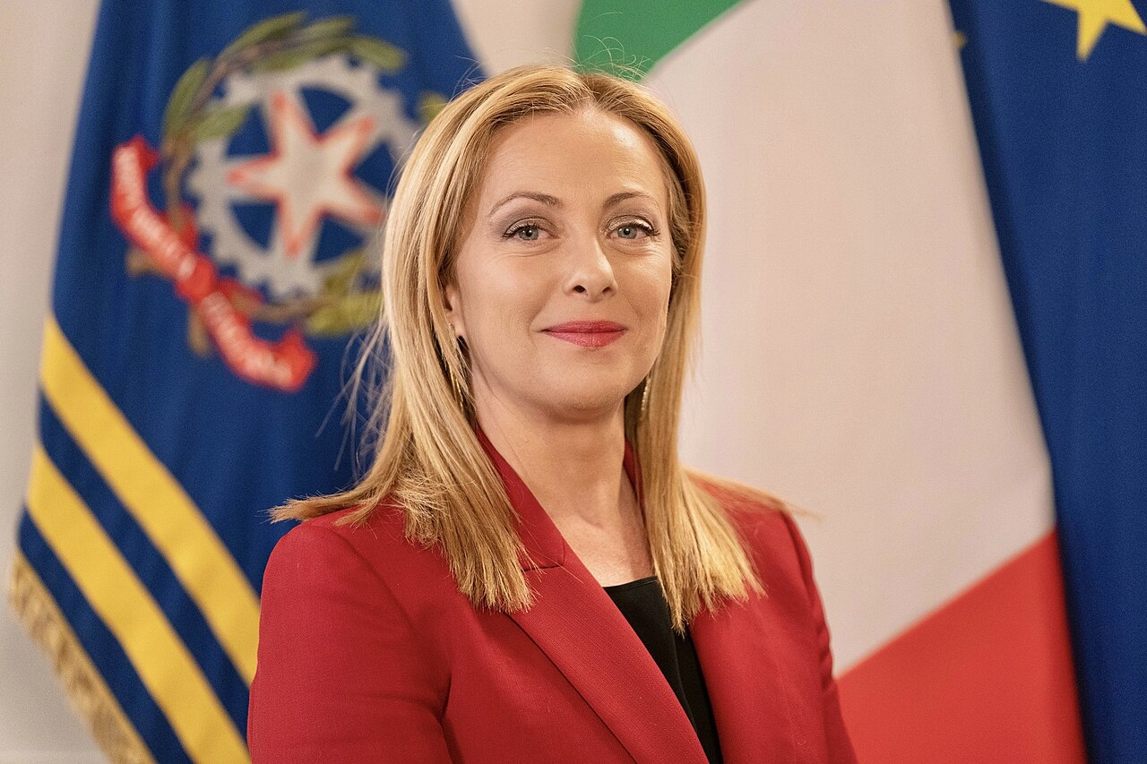 Una foto ufficiale di Giorgia Meloni sorridente con la bandiera dell'Italia alle spalle