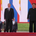 Vladimir Putin e Kim Jong Un in posa, dietro di loro alcuni funzionari della Corea del Nord e un militare sullo sfondo. Accanto a Putin c'è una bandiera della Russia