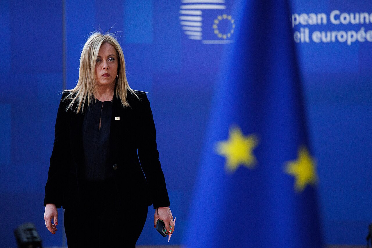 La presidente del Consiglio italiana Giorgia Meloni cammina, sullo sfondo la bandiera dell'Unione Europea