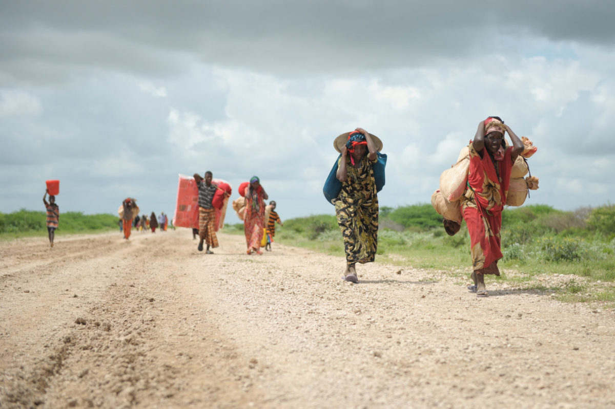 Donne, che camminano con ciò che riescono a portare, diretto verso un campo per sfollati eretto accanto a una base militare per le vittime delle forti piogge a causa della crisi climatica.