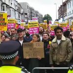 Un gruppo nel Regno Unito di manifestanti venuti a difendere le proprie comunità contro gli attacchi razzisti degli scorsi giorni. di fronte al cordone di poliziotti, reggono cartelloni con varie scritte: "smash fascism and racism" "Farage and EDL not welcome here" "refugee welcome" "stop the far-right"