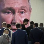 Tanti cittadini russi in primo piano e sullo sfondo il volto di Putin proiettato in uno schermo. L'opposizione a Putin in Russia non riesce a organizzarsi.