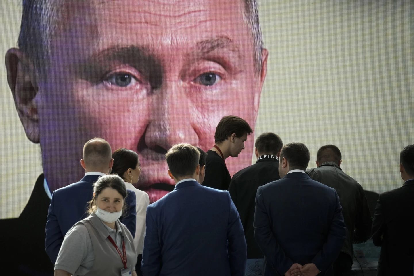 Tanti cittadini russi in primo piano e sullo sfondo il volto di Putin proiettato in uno schermo. L'opposizione a Putin in Russia non riesce a organizzarsi.