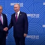 António Guterres e Vladimir Putin si stringono, sullo sfondo un pannello blu con i loghi del Summit Brics