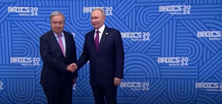 António Guterres e Vladimir Putin si stringono, sullo sfondo un pannello blu con i loghi del Summit Brics