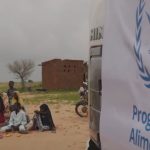 Alcuni rifugiati del Sudan seduti in cerchio vicino a un camione del World Food Programme