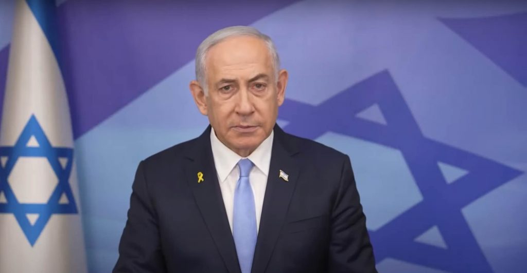 Il premier israeliano Netanyahu in un discorso pubblico. Accanto la bandiera di Israele