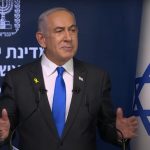 Benjamin Netanyahu durante una conferenza stampa, alle sue spalle la bandiera israeliana