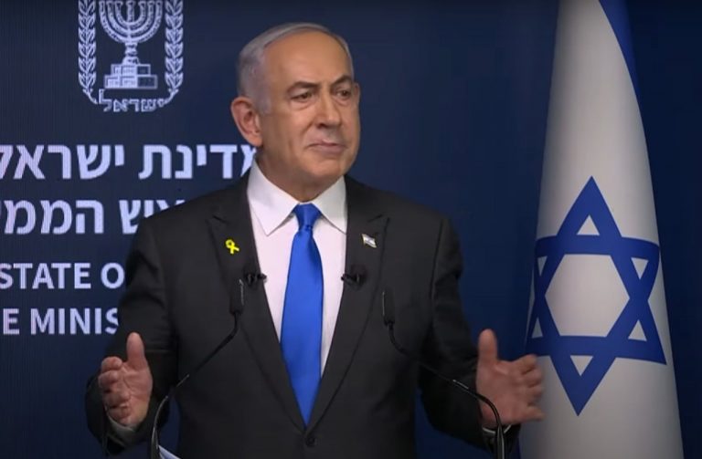 Benjamin Netanyahu durante una conferenza stampa, alle sue spalle la bandiera israeliana