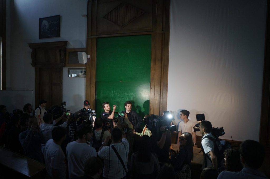 Manifestanti dentro un'aula universitaria, alla cattedra attorniata da giornalisti con telecamere e microfoni. La lavagna alle loro spalle ha una scritta in geogiano: "no alla legge russa". 