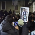 Un uomo col megafono parla a una folla con la foto di Ramy Elgaml, morto dopo un inseguimento dei carabinieri nel quartiere Corvetto, a Milano.