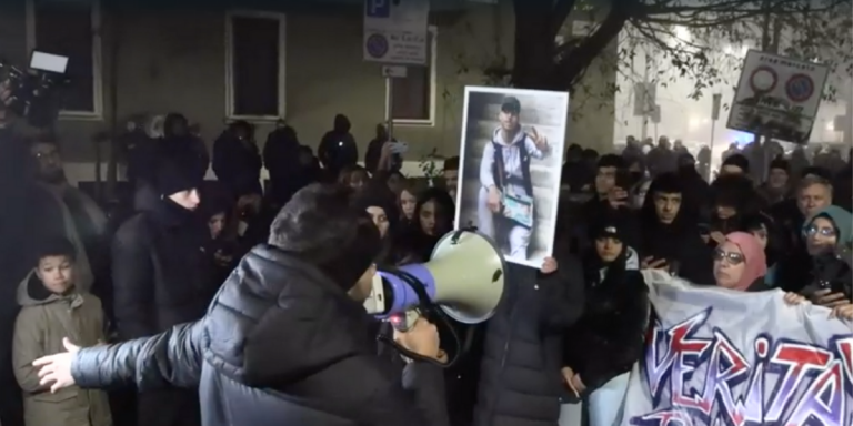 Un uomo col megafono parla a una folla con la foto di Ramy Elgaml, morto dopo un inseguimento dei carabinieri nel quartiere Corvetto, a Milano.