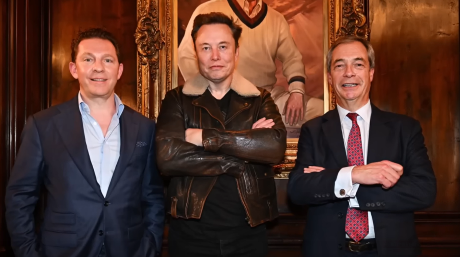 Elon Musk a braccia incrociate in mezzo a due persone (alla sua sinistra Nigel Farage). Dietro di loro un ritratto di Donald Trump