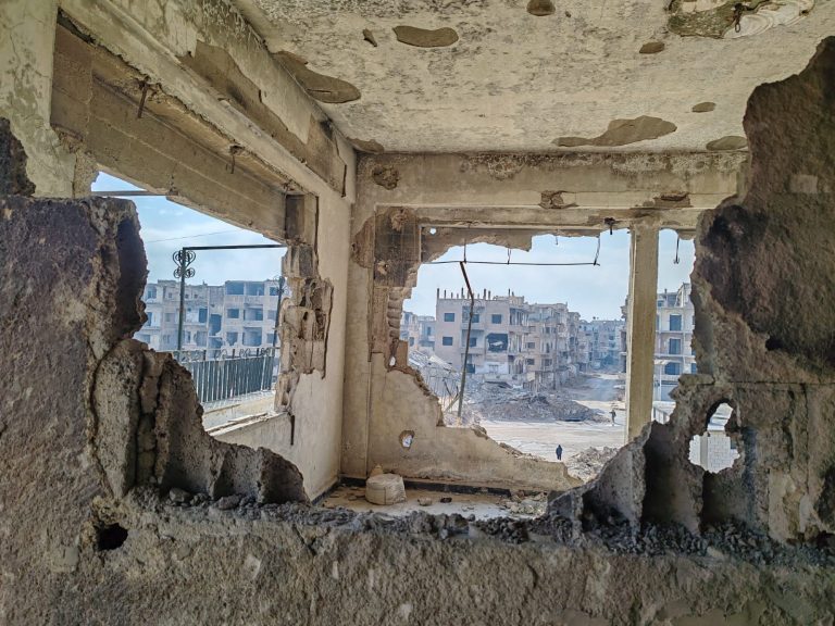 Dall'interno di un'abitazione distrutta si vedono sullo sfondo altre abitazioni nel centro di Harasta, in Siria.