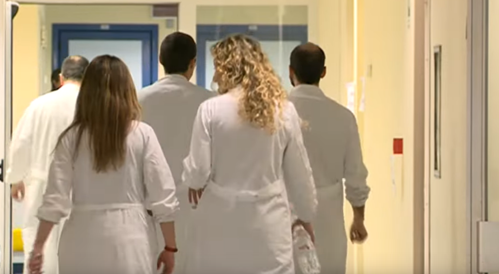 Un gruppo di 4 medici, di spalle, mentre cammina in un corridoio d'ospedale. La sanità italiana è in crisi.