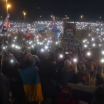 una folla di manifestanti in Slovacchia. Alcuni hanno bandiere del paese, altri dell'Ucraina. Il buio della sera è illuminato dagli schermi degli smartphone dei manifestanti, che li impugnano come fiaccole