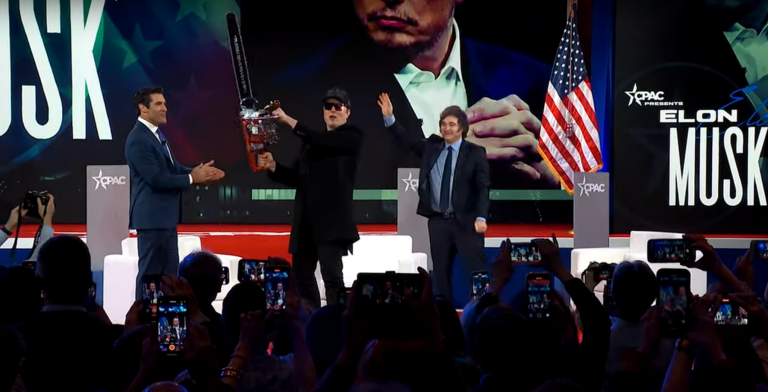 Musk imbraccia una motosega accanto al presidente argentino Javier Milei, sul palco della conferenza CPAC. In primo piano si vede la prima fila del pubblico che filma o fotografa con gli smartphone.