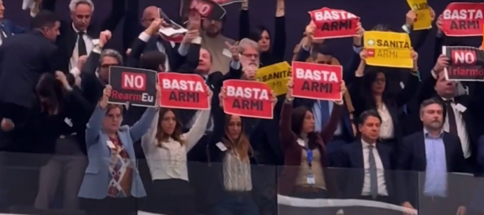 M5S MEPs raising signs (“no more weapons, ‘no rearmEU’, + healthcare - weapons”)