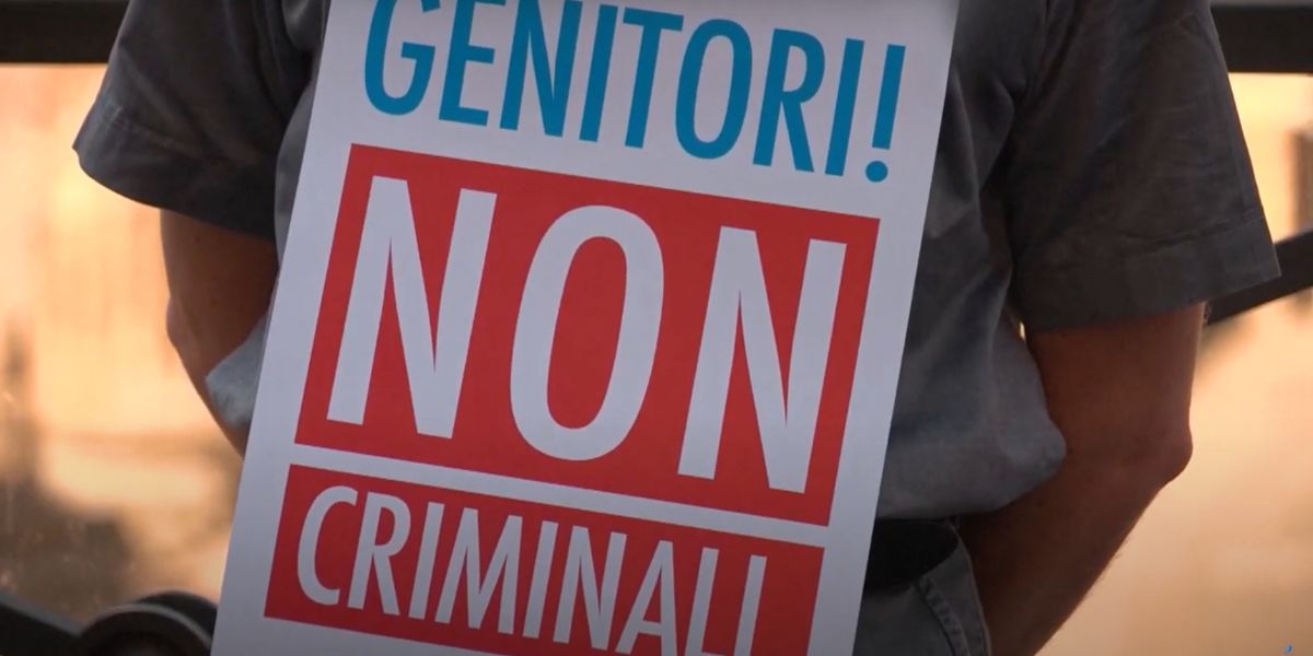 Un cartello con la scritta "Genitori! Non criminali." esposto da un manifestante contro la legge che punisce la GPA come reato universale